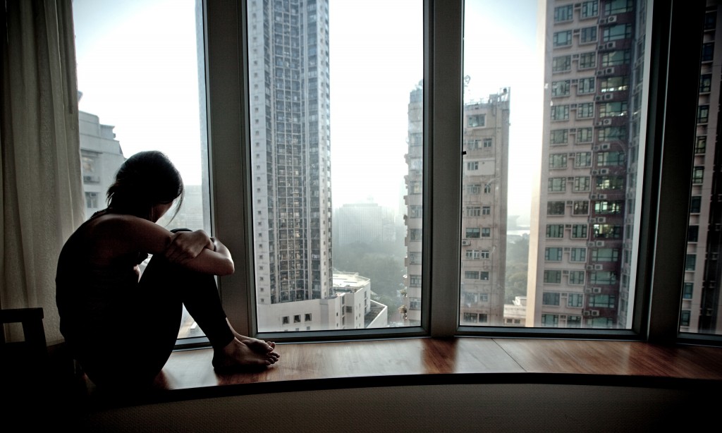 A lonely girl looking out of a high-rise flat.